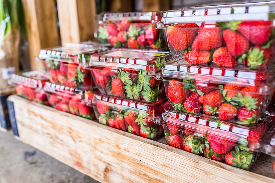 A stack of clear plastic containers with red strawberries inside